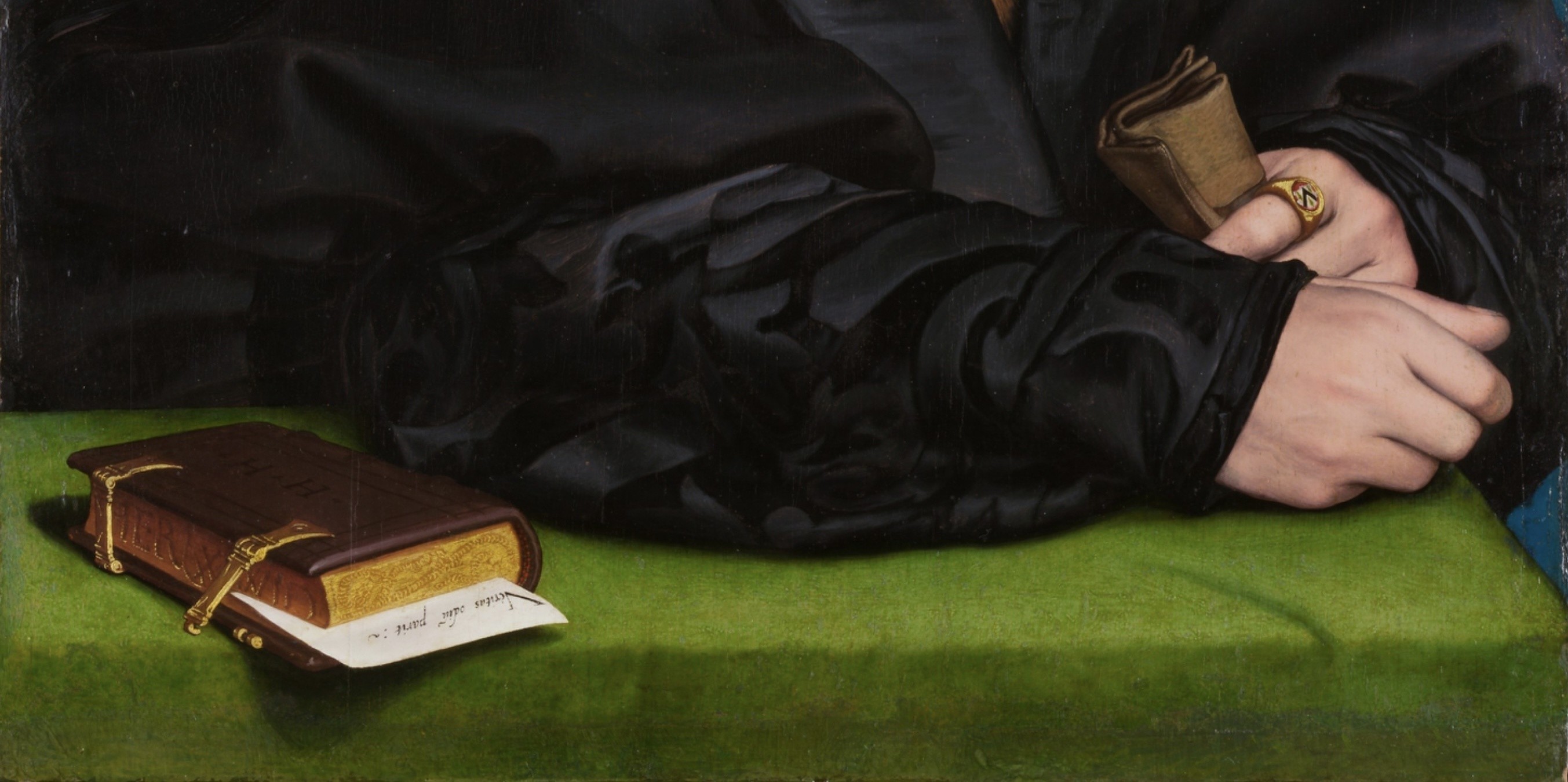 Detail of Holbein’s portrait: the sitter’s clasped hands with a gold signet ring bearing his arms, a pair of gloves, and a clasped book on a green cloth with a note inscribed Veritas odium parit.